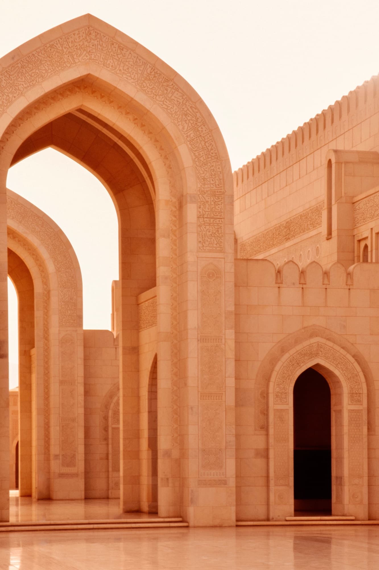 Warm sandstone arches carved with calligraphic bands, in golden light.
