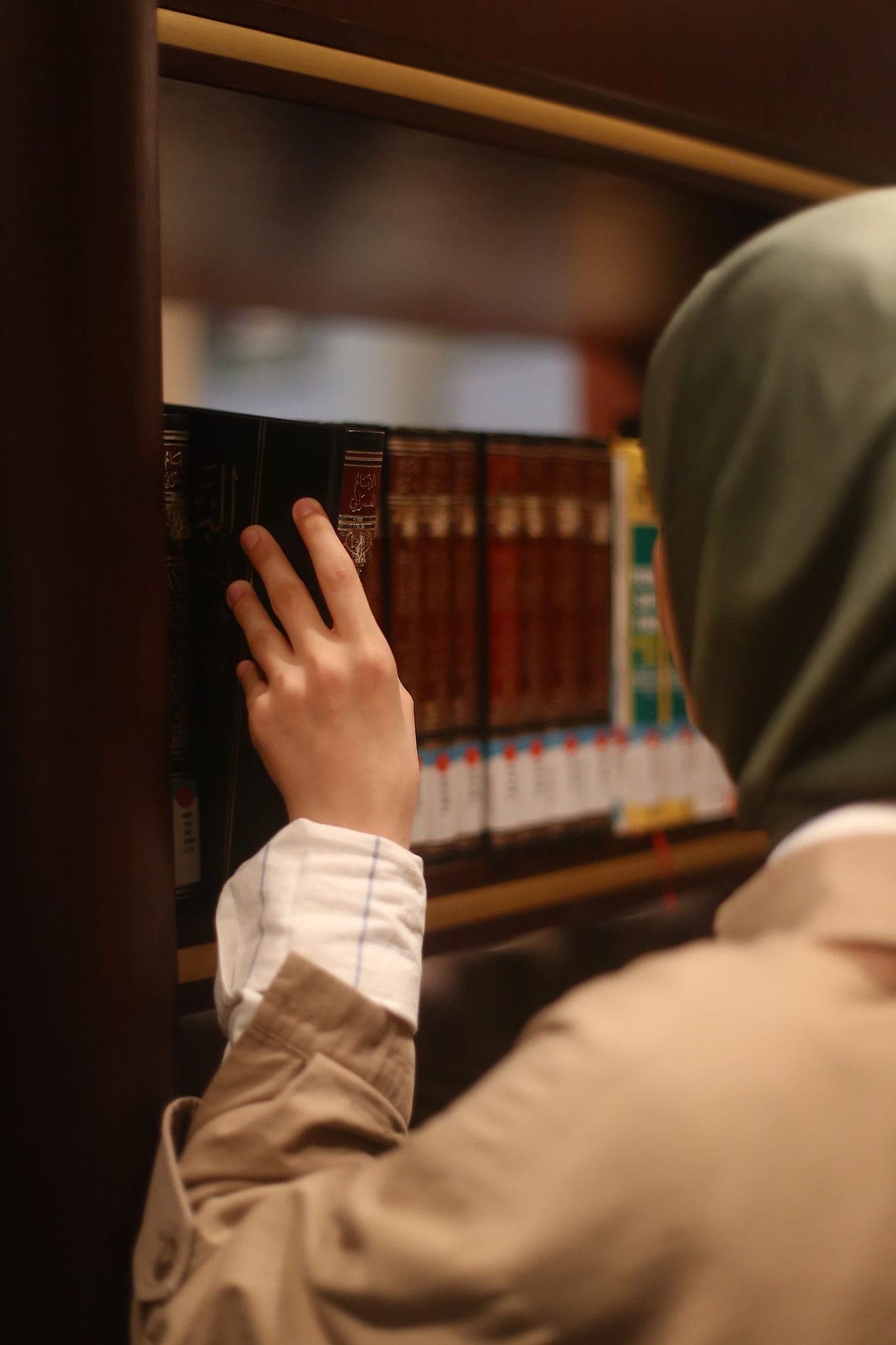 A hand reaching for a book on an open shelf.